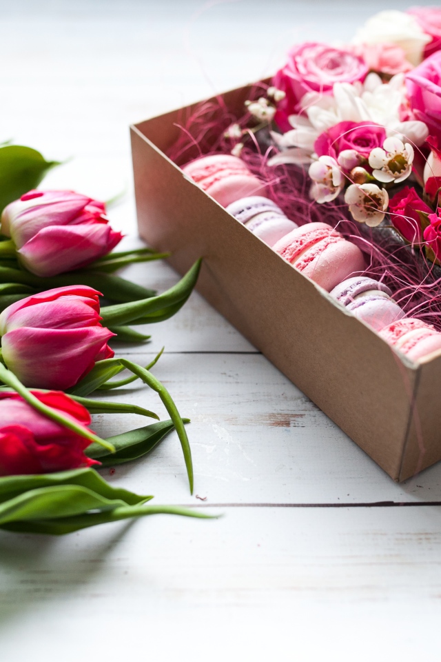 Букет розовых тюльпанов на столе с коробкой печенья макарон и цветами