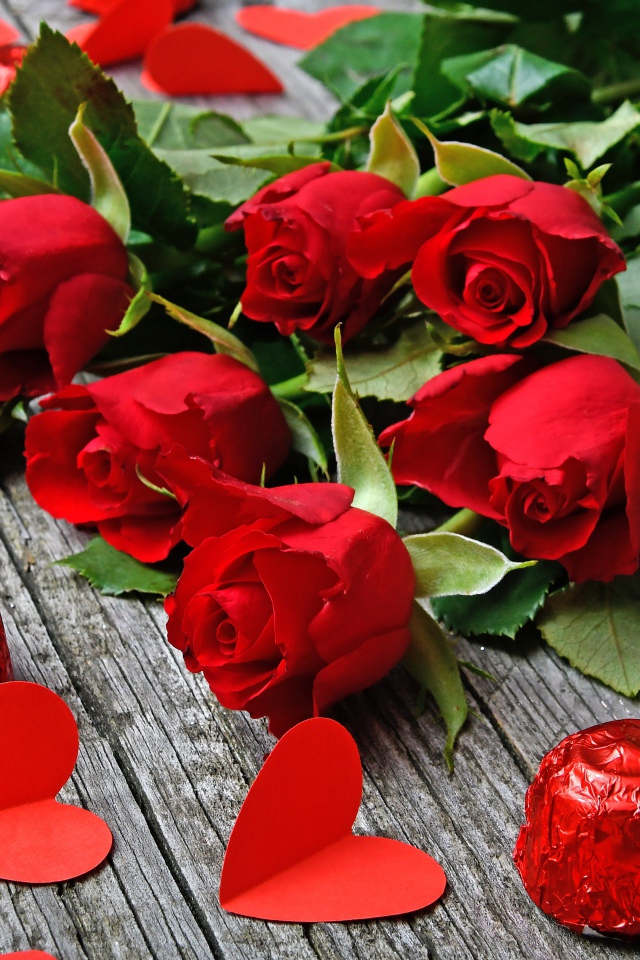 Букет красных роз на деревянном столе с конфетами и красными сердечками