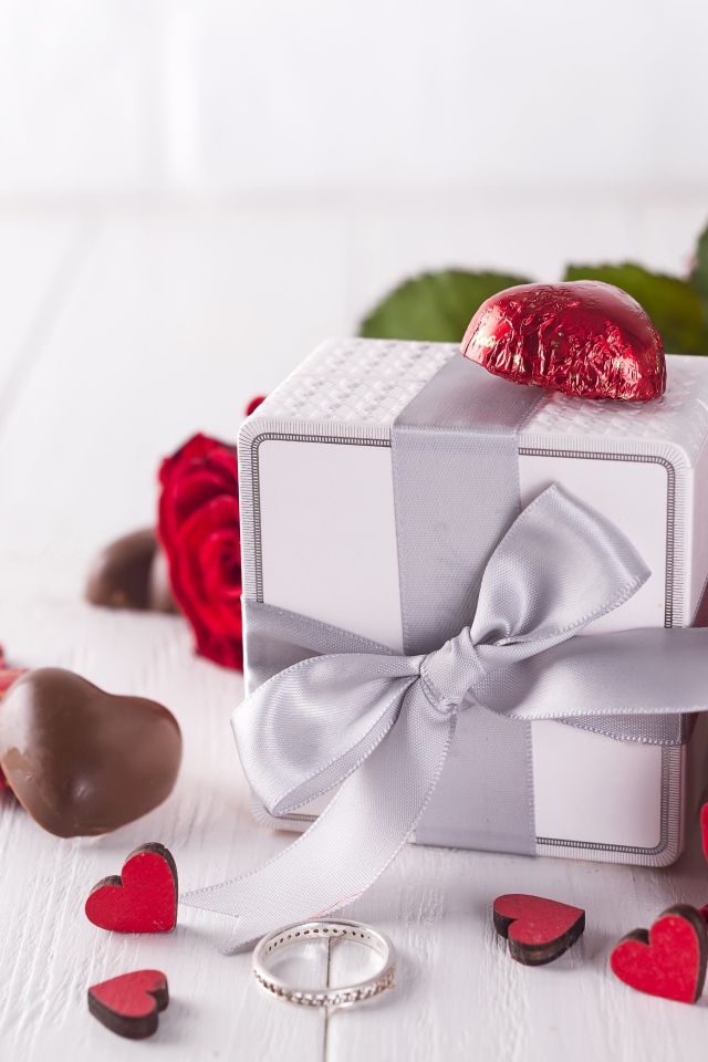 Подарок на столе с конфетами и букетом красных роз 