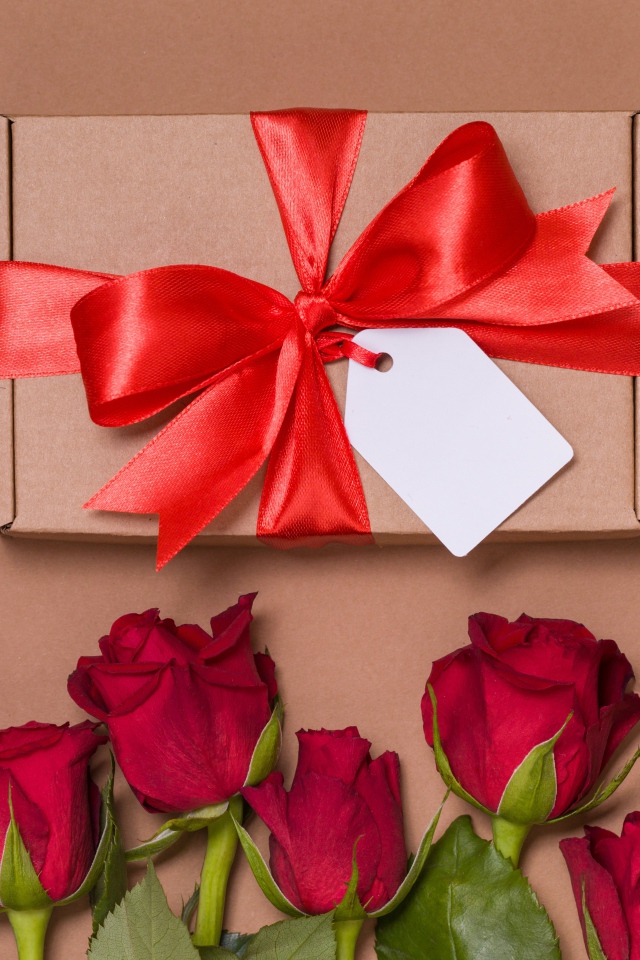 Подарок с красным бантом на бежевом фоне с красными розами