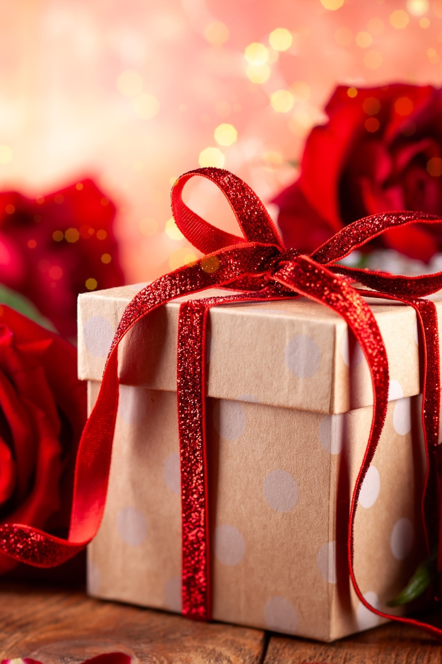 Подарок с красным бантом на столе с букетом роз