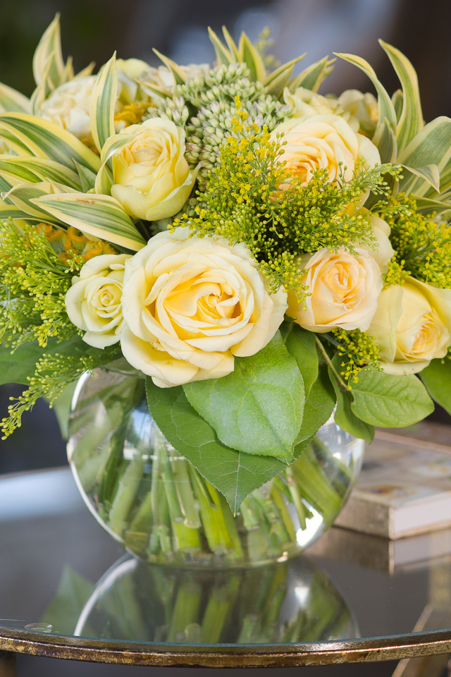 Красивый букет роз с зелеными листьями в в вазе на стеклянном столе