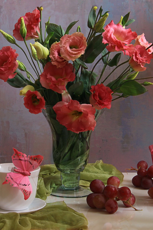 Букет розовых цветов эустомы на столе с виноградом