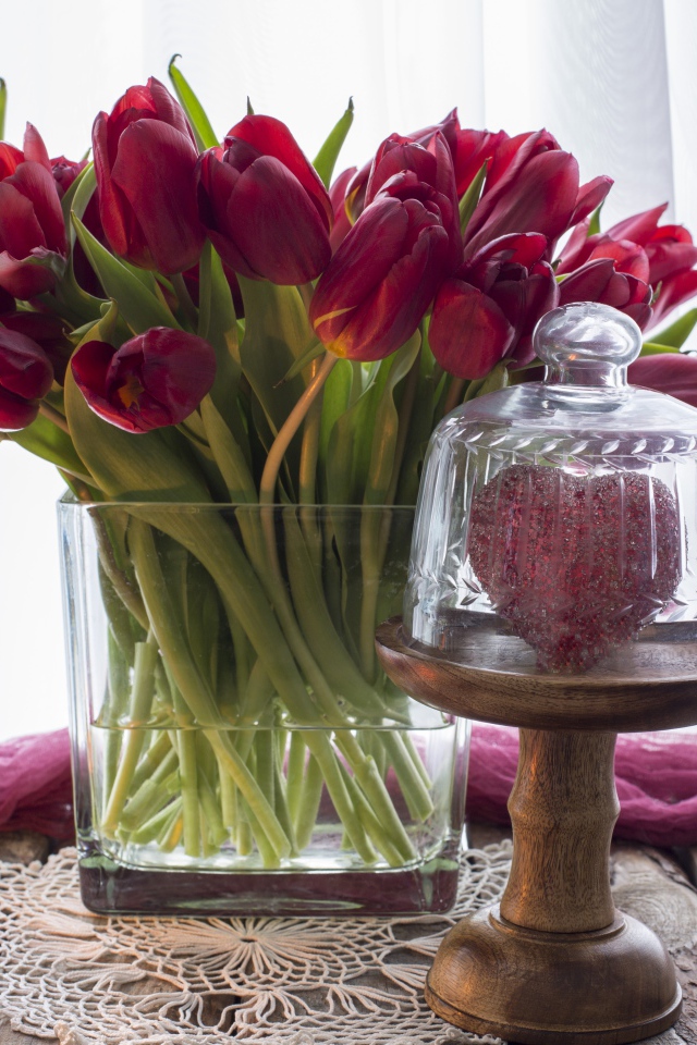 Букет красных тюльпанов в стеклянной вазе на столе со свечой и сердцем 