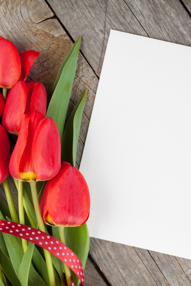 Букет красных тюльпанов с листом бумаги на деревянном столе
