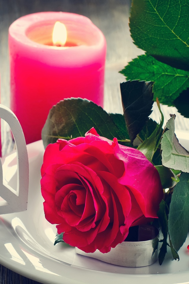 Красная роза на белой тарелке с сердечками на столе с зажженными свечами