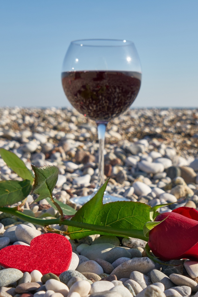 Красная роза на морской гальке с сердечком и бокалом вина