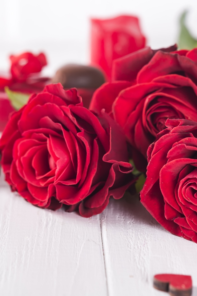 Три красивые красные розы на столе с конфетами