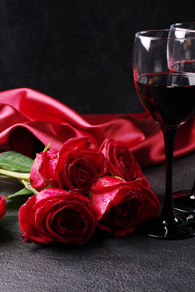 Два бокала с красным вином на черном фоне с букетом красных роз