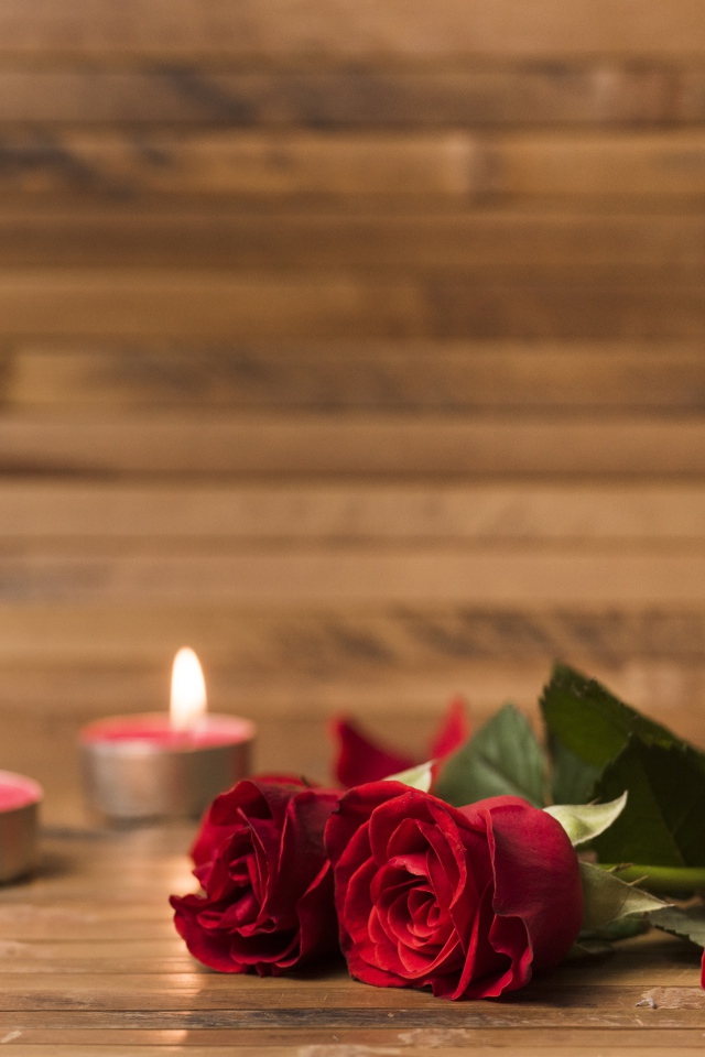 Две красные розы на столе с зажженными свечами 