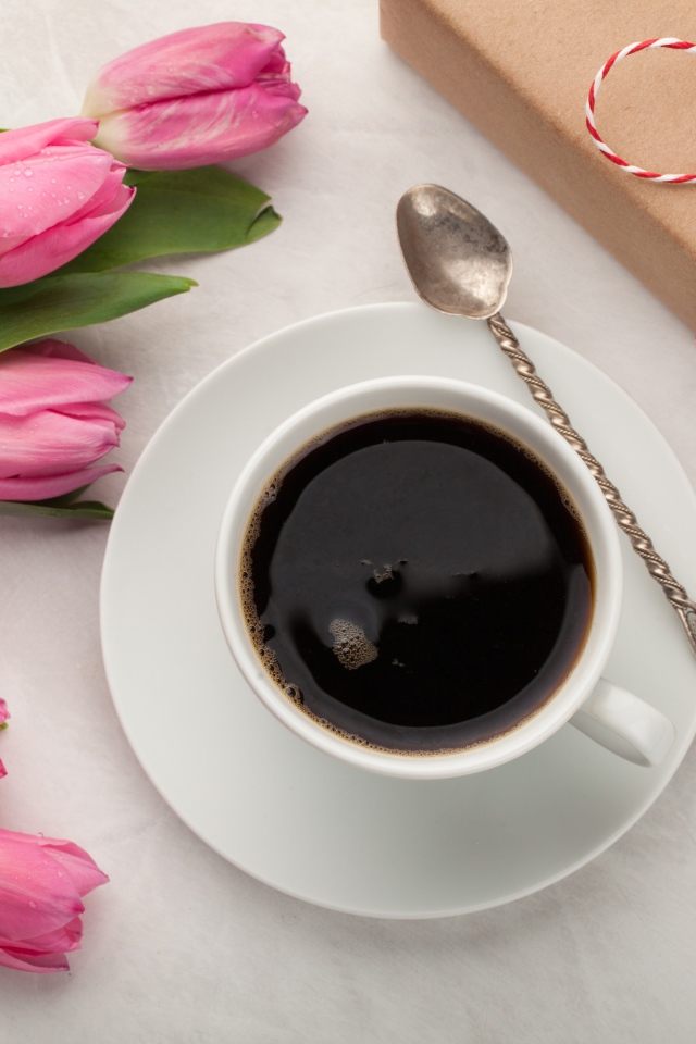 Белая чашка кофе на столе букетом розовых тюльпанов и подарком