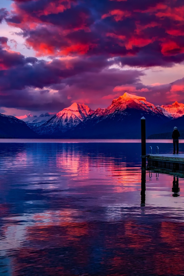 Beautiful sunset in the sky over the tops of snow-capped mountains by the lake