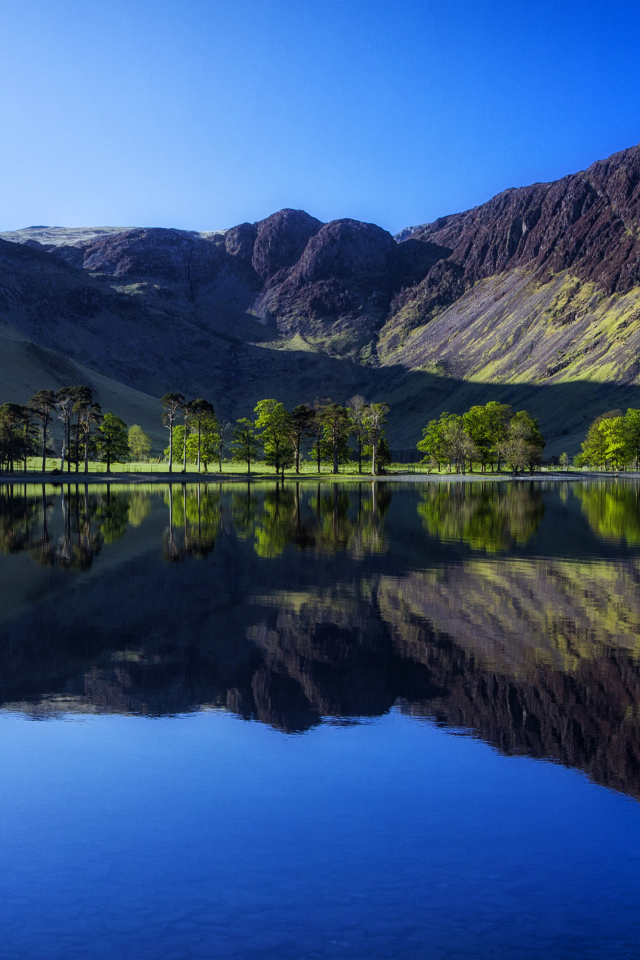 Черные высокие горы с голубым небом отражаются в воде озера