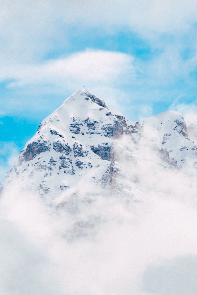 Заснеженная вершина горы в белых облаках под голубым небом