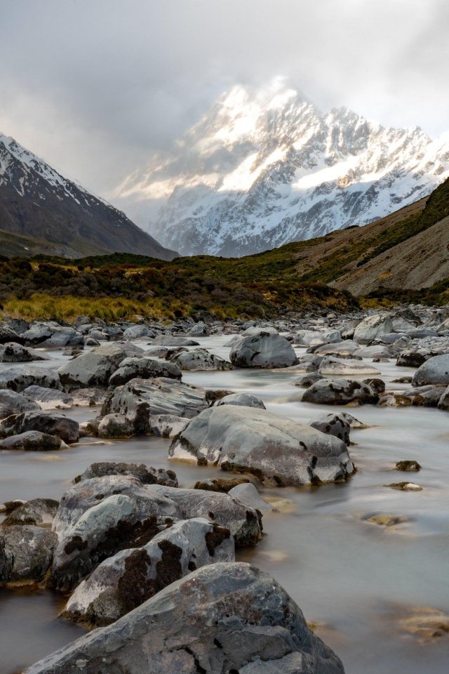Камни в воде у заснеженных гор 