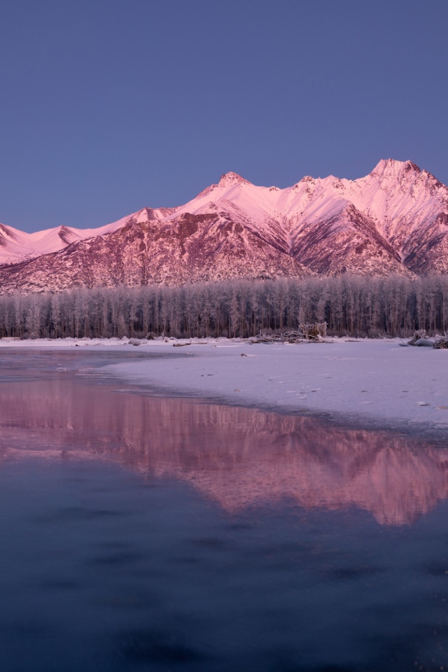 The moon over the snow-capped mountains is reflected in the icy lake