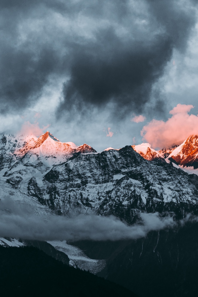 Солнце на рассвете освещает вершины заснеженных гор 