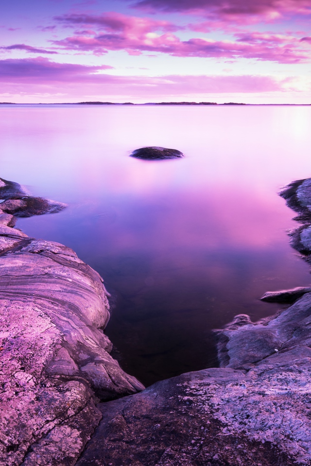 Сиреневый закат в небе над водой и камнями