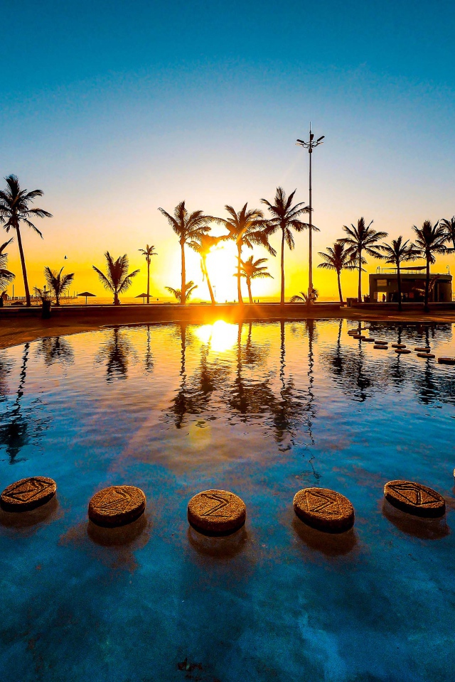 Закат солнца на тропическом пляже на фоне бассейна