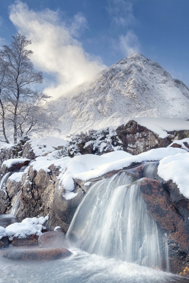 Водопад стекает с камней на фоне заснеженной горы