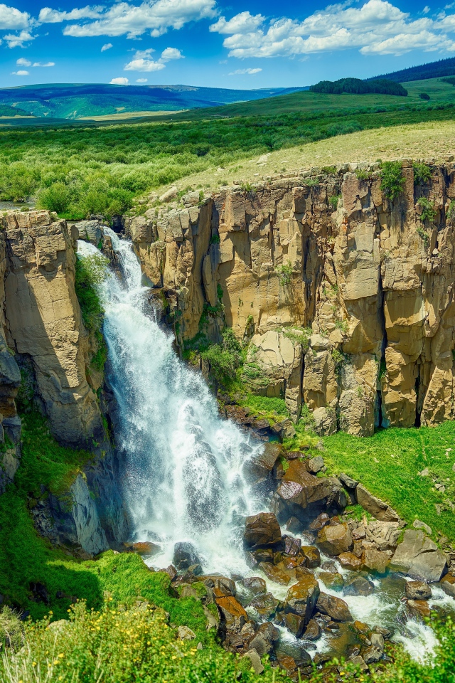 Быстрая вода водопада стекает по утесу на фоне голубого неба