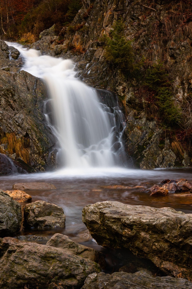 Быстрая вода водопада стекает по камням в горную реку
