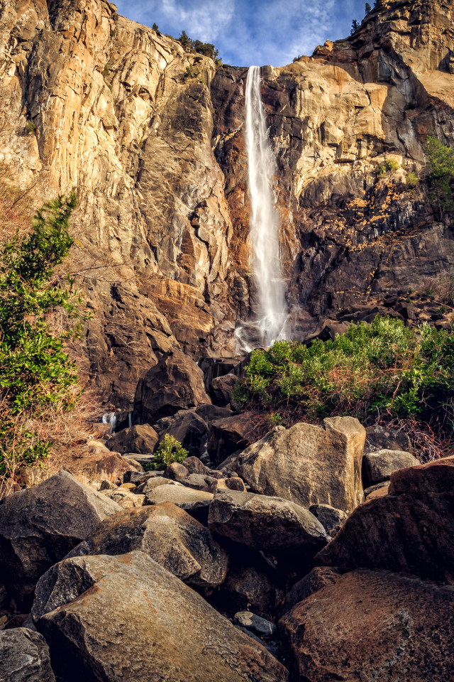 Водопад стекает с высокой скалы на камни 