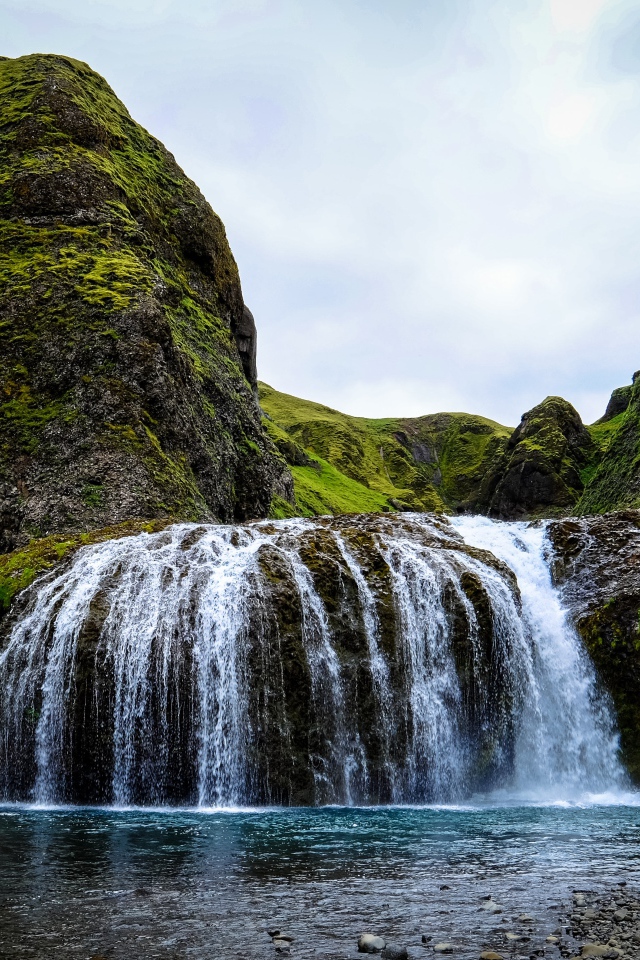 Белая вода водопада стекает по покрытым мхом скалам