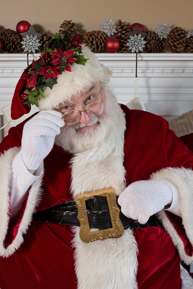 Санта Клаус в очках сидит у камина у новогодней елки