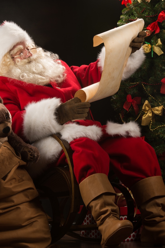 Санта Клаус с мешком подарков читает у елки