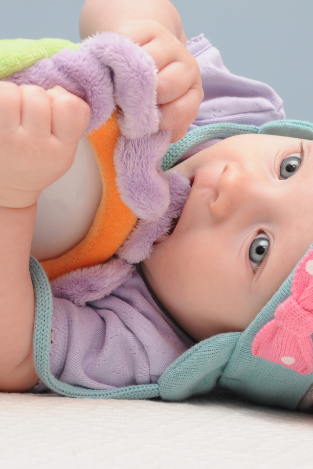 Младенец в шапке грызет мягкую игрушку