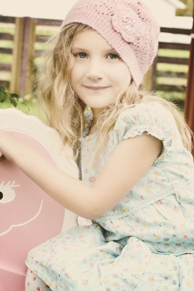 Девочка в платье сидит на деревянной лошади