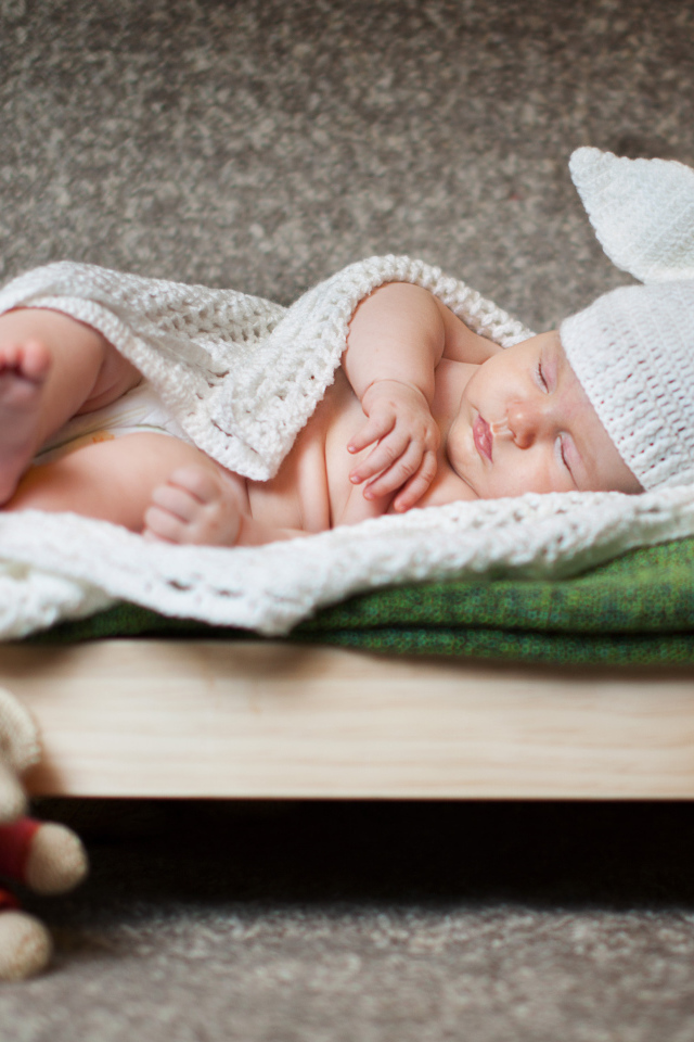 Маленький спящий ребенок в шапке с ушками спит на кровати