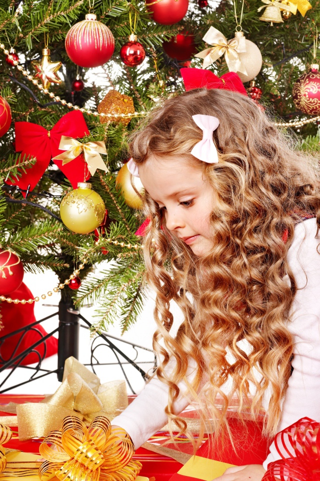 Красивая маленькая девочка смотрит подарки под елкой на новый год 