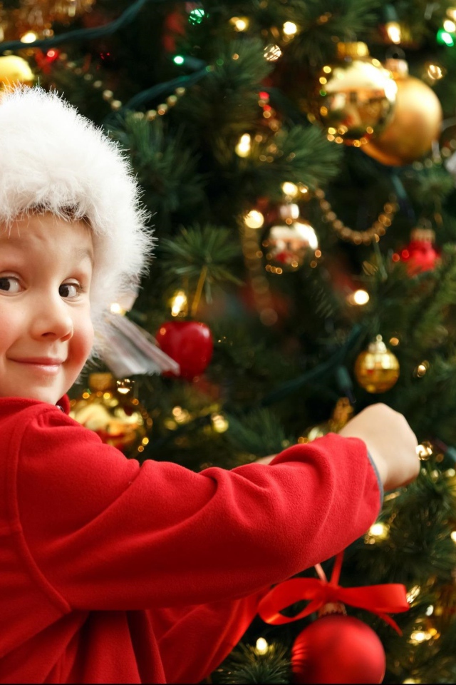 Мальчик в шапке Санта Клауса наряжает елку