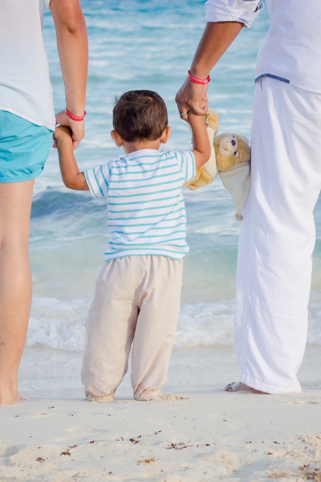 Семья с маленьким ребенком идет по пляжу