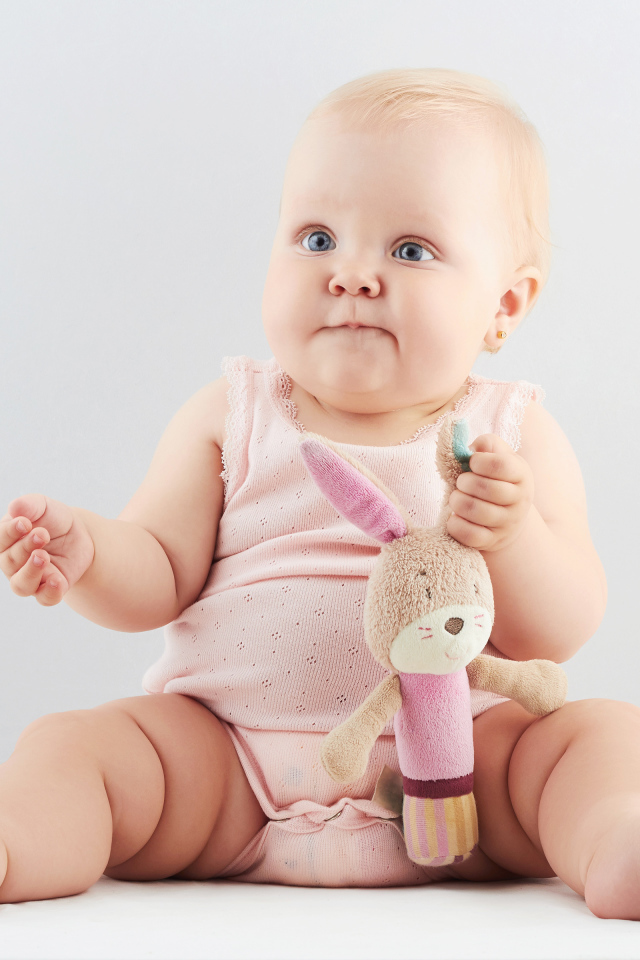 Смешной малыш с игрушкой сидит на сером фоне