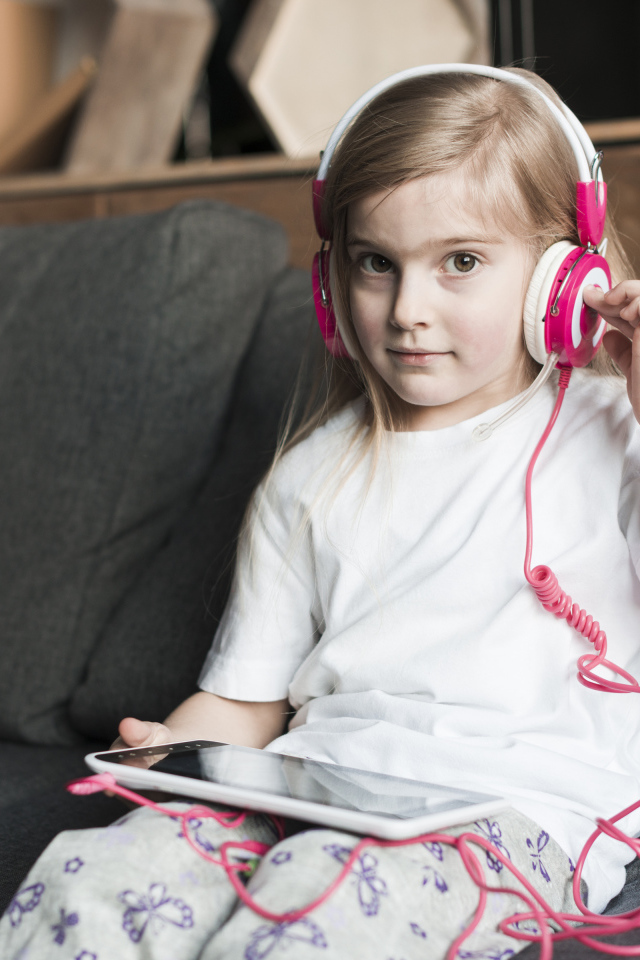 Девочка сидит на диване в наушниках  и с планшетом