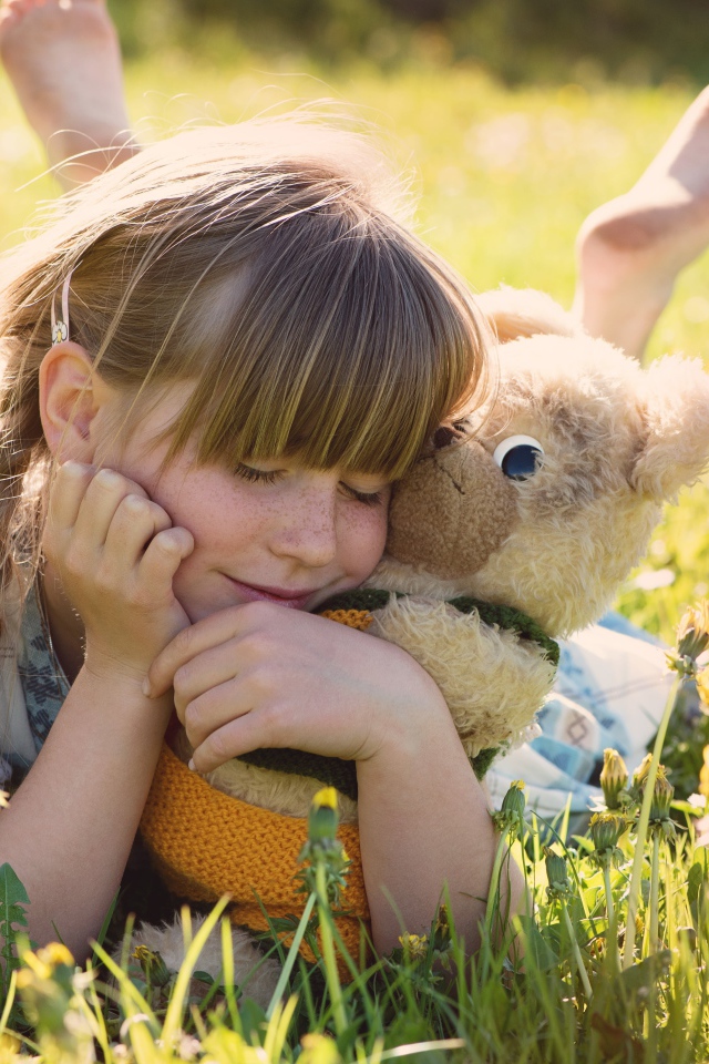 Девочка с игрушкой в руках лежит на траве 