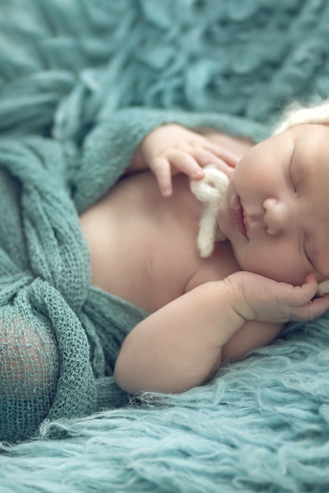 Маленький ребенок в вязаной шапке спит на меховом покрывале