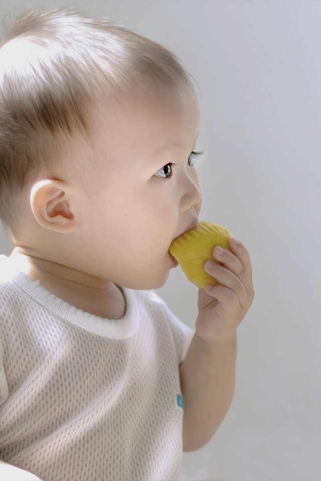 Маленький ребенок грызет игрушку на сером фоне