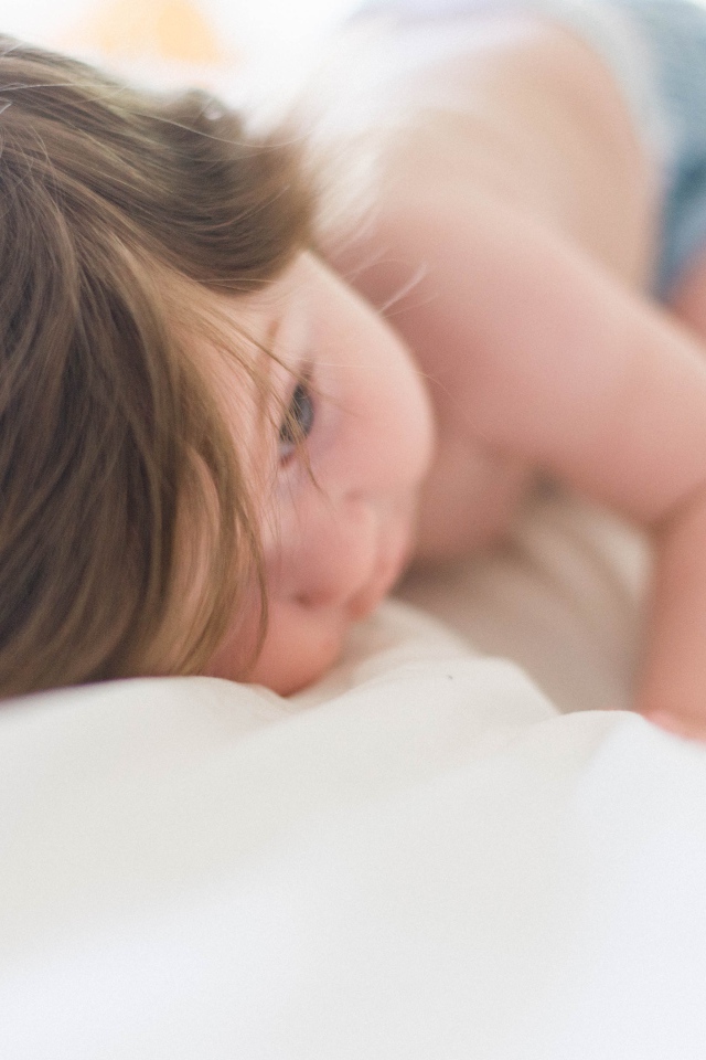 Маленький ребенок с русыми волосами лежит на кровати