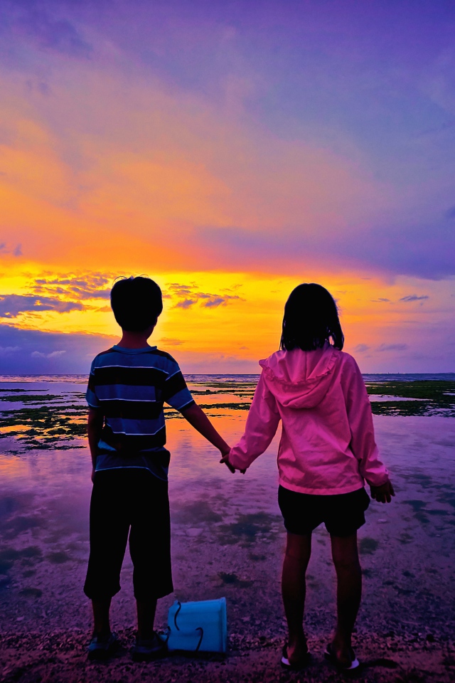 Маленькие мальчик и девочка стоят у воды на фоне заката 