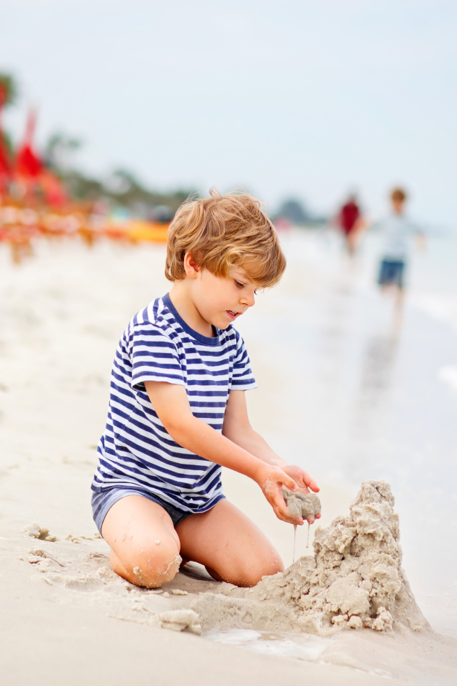 Маленький мальчик строит замок из песка на пляже