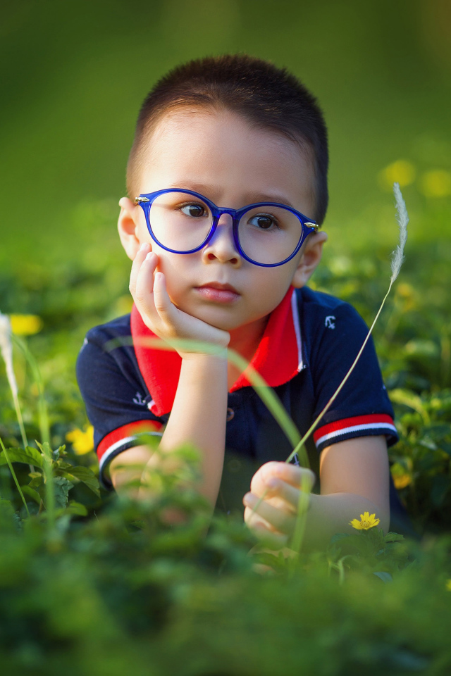 Маленький мальчик в очках лежит на зеленой траве