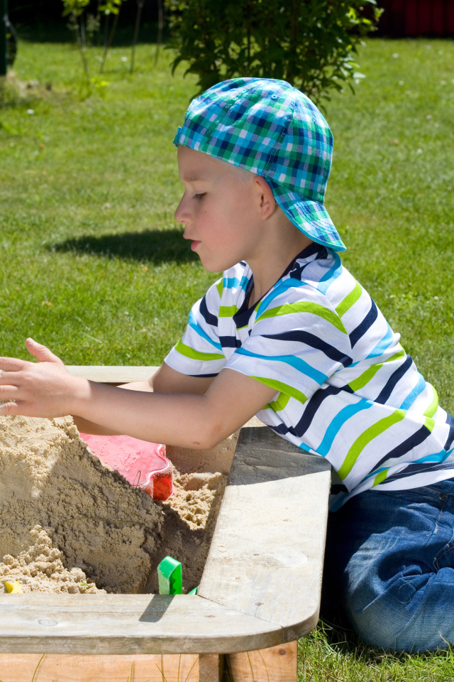 Маленький мальчик играет в песке на зеленой траве