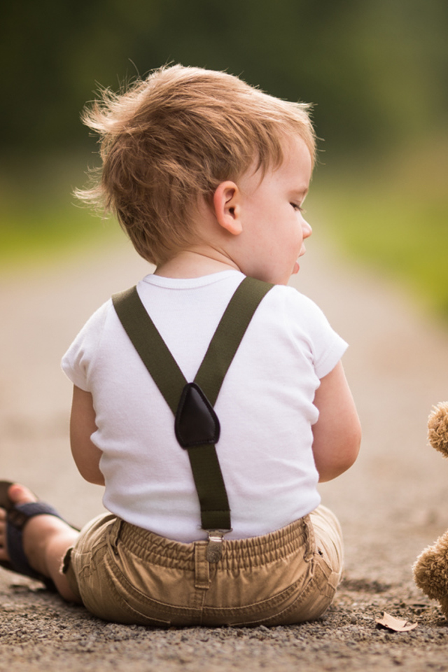 Маленький мальчик сидит на дороге с игрушечным мишкой