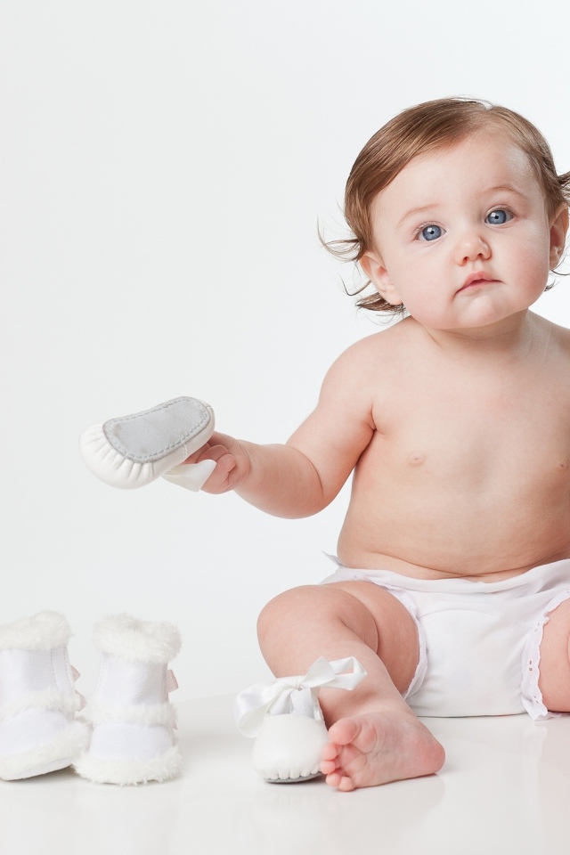 Маленький забавный голубоглазый малыш с обувью на белом фоне