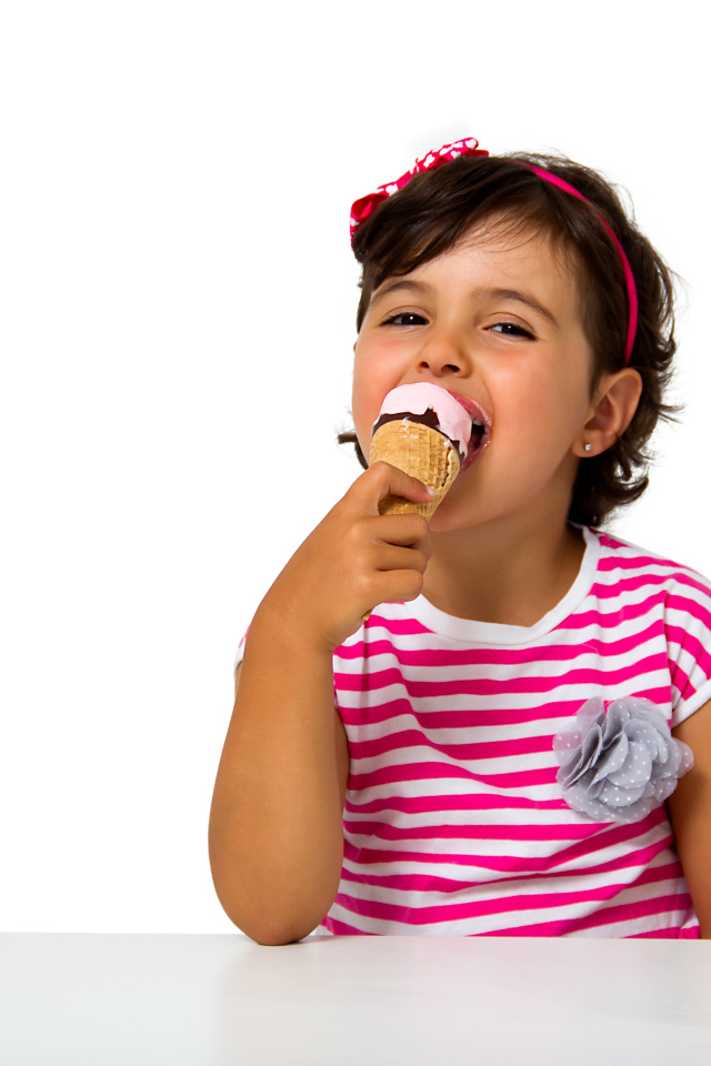 Маленькая девочка ест мороженое за столом на белом фоне