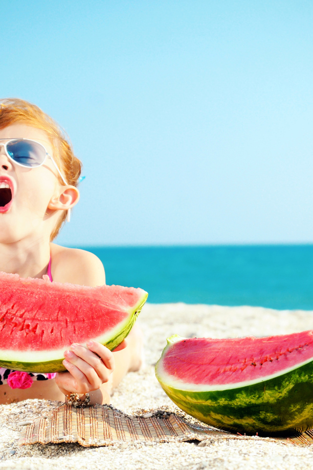 Маленькая девочка ест арбуз на песке у моря